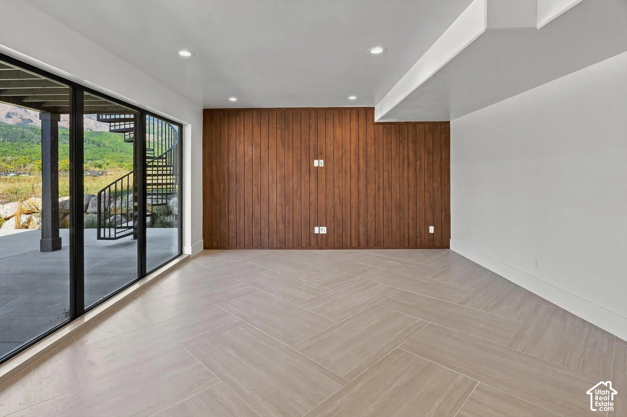 Full-height sliding glass doors, chevron-patterned tile flooring, recessed ceiling lighting, and a textured wood-panel accent wall