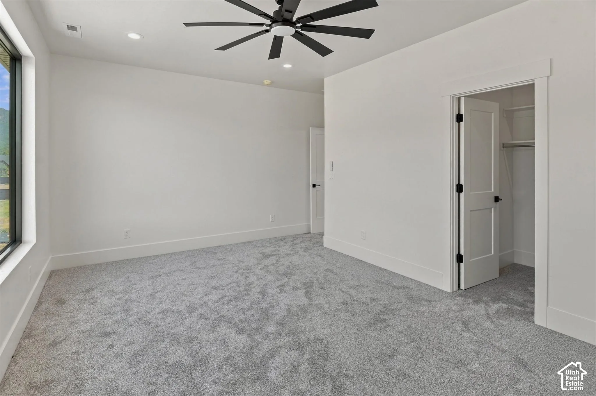 Recessed lighting, large window, gray carpeting, matte black ceiling fan, and white interior doors