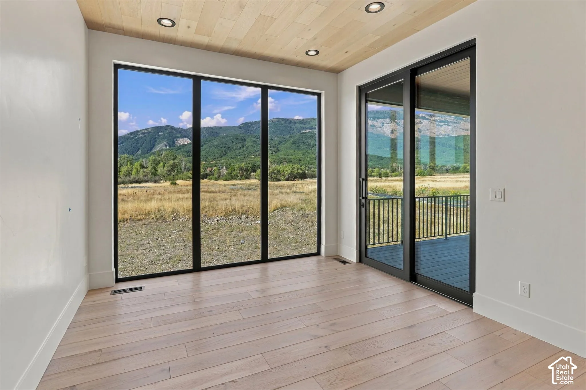 Wood-finish flooring with a light tone, black-framed sliding glass door, recessed lighting, and a wood-finish ceiling
