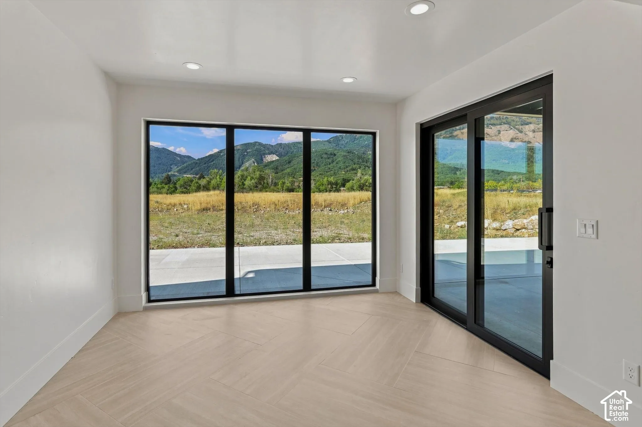 Recessed lighting, wood-finish flooring, full-height windows, and a sliding glass door provide natural illumination and mountain scenery
