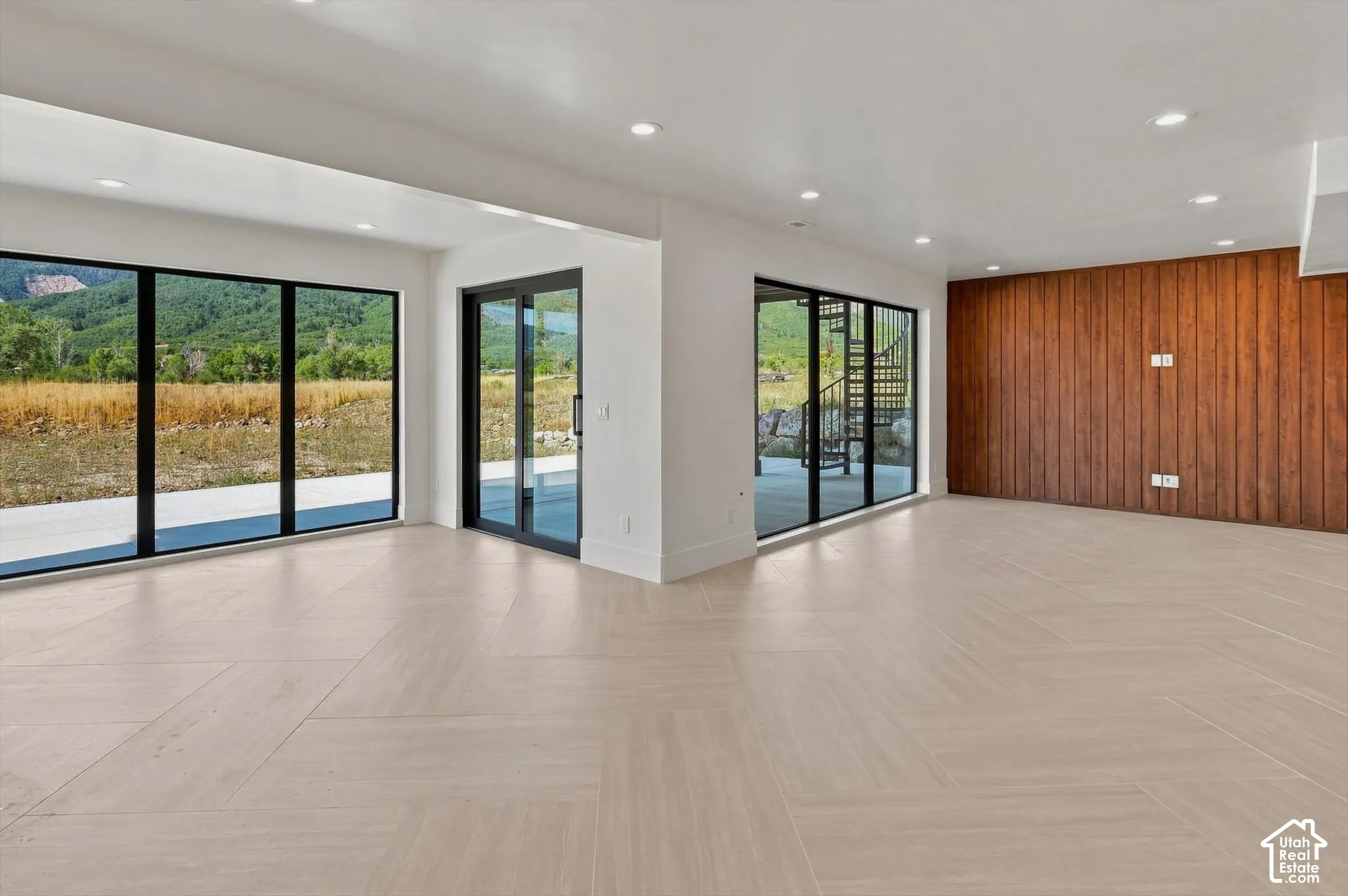 Expansive room featuring multiple full-height glass panels, glass sliding doors, recessed ceiling lighting, and a wood-paneled accent wall
