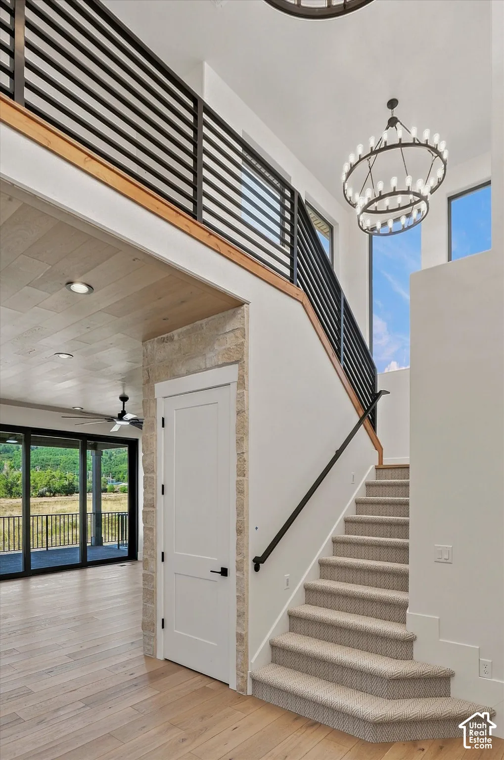 Open-concept living area with wood-finish flooring, a contemporary staircase featuring carpeted treads, a black metal handrail, and a stone-clad doorway