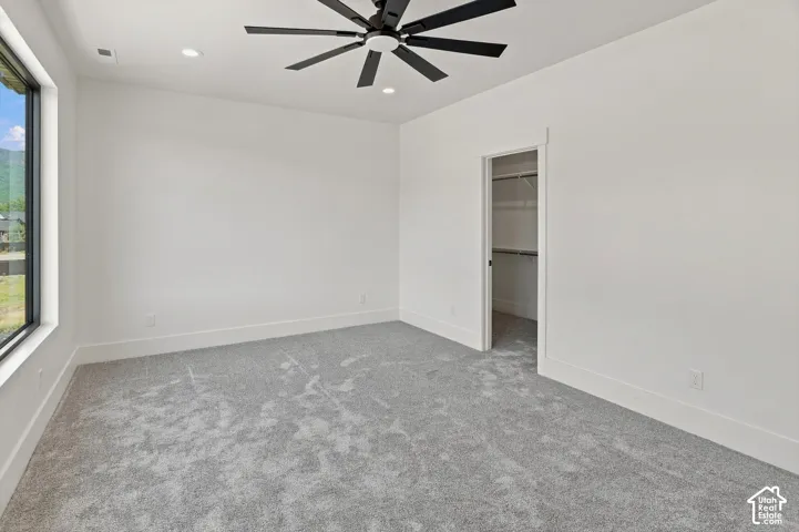 Spacious room featuring a contemporary ceiling fan, recessed lighting, expansive window, closet with built-in shelving, and light gray carpeting