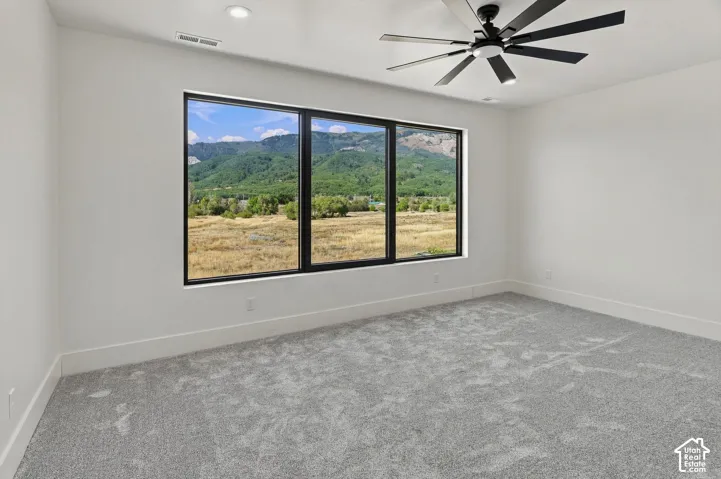 Expansive picture windows framing mountain scenery, modern ceiling fan with integrated lighting, recessed lighting, neutral wall finishes, and light-toned carpeting