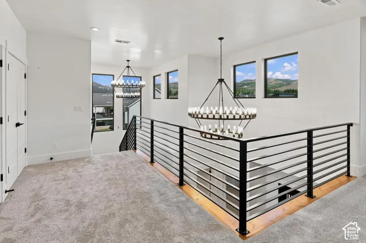 Carpeted landing with modern chandeliers, black metal horizontal bar railing, and multiple windows