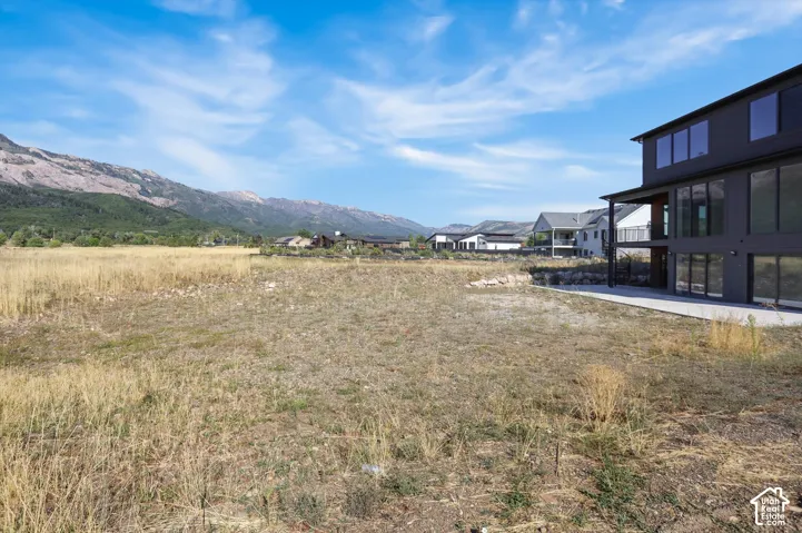 Expansive lot featuring a contemporary residence with large windows, an exterior balcony, and a mountainside backdrop