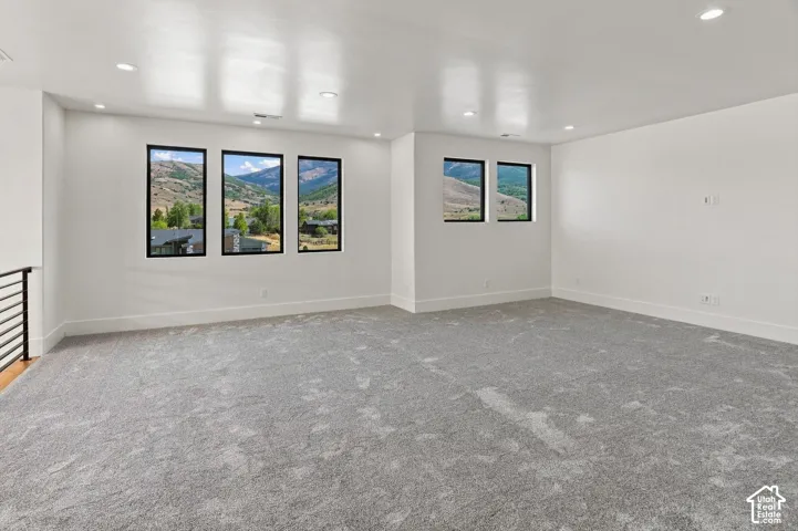 Spacious room featuring gray textured carpeting, white walls, recessed ceiling lighting, and multiple windows with black frames