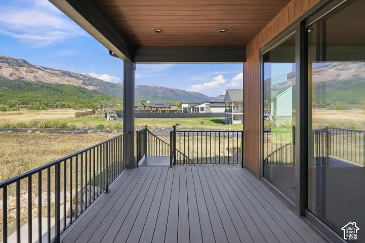 Expansive covered deck with composite decking, black metal railing, mountain scenery, and a sliding glass door
