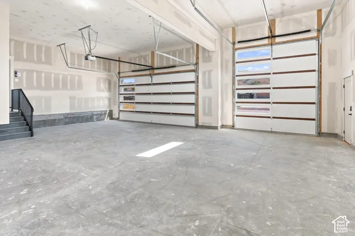 Two garage doors with horizontal window inserts, concrete flooring, and a staircase with a black metal handrail