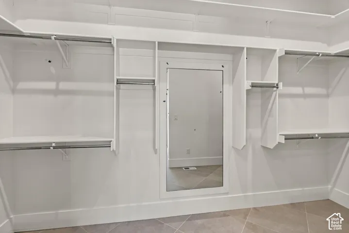 Custom closet system with multiple shelving units and hanging rods, integrated full-length mirror, and tiled flooring