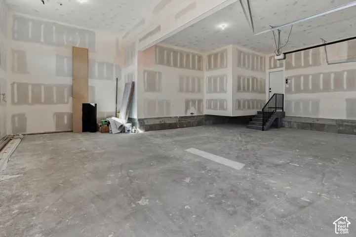 Spacious garage with concrete flooring, interior staircase, and direct entry door
