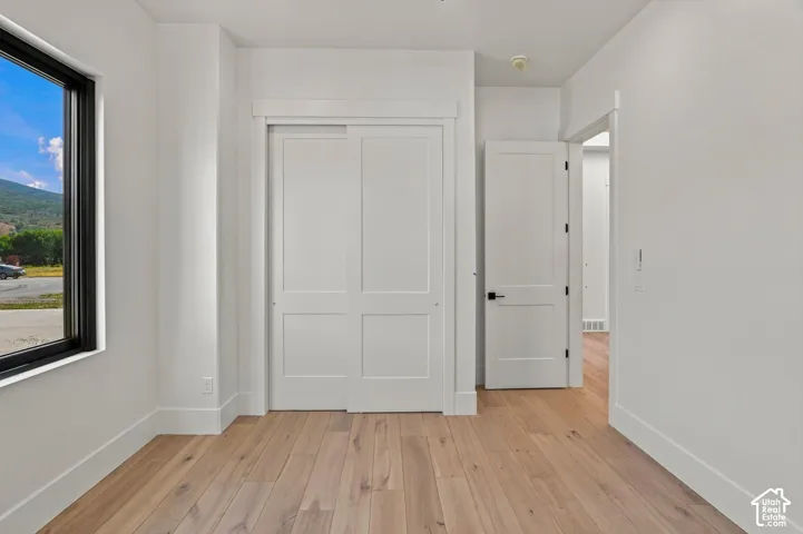 Wood-finish flooring throughout, bright white walls, large window with black trim, and a white sliding closet door