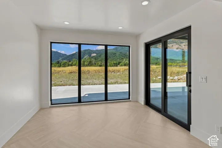 Recessed lighting, wood-finish flooring, full-height windows, and a sliding glass door provide natural illumination and mountain scenery