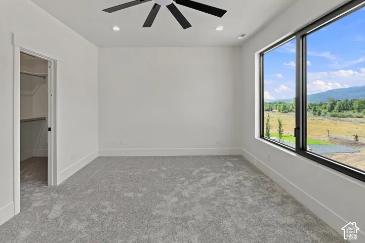 Expansive window with black framing, recessed lighting, ceiling fan with black blades, and light gray carpeted flooring