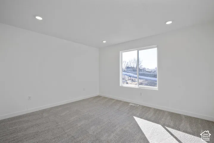 Recessed lighting, light-colored walls, large window with white frame, and gray carpet flooring