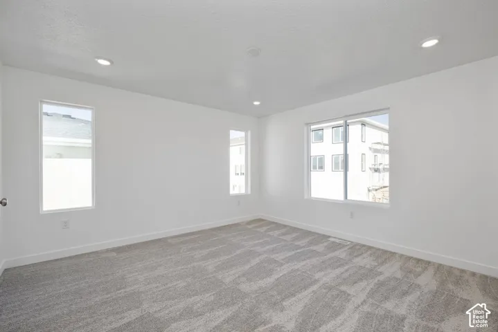Recessed lighting, light gray patterned carpet, multiple windows, and white walls