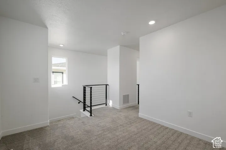 Recessed lighting, carpeted flooring, white walls, and a modern metal railing