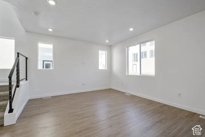 Wood-finish flooring with white baseboards, recessed lighting, and a modern staircase featuring black metal railings