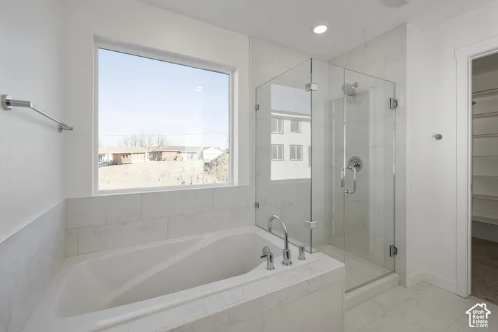 Soaking tub with deck-mounted chrome fixtures, glass-enclosed shower with a rainfall showerhead, and white tiled surround