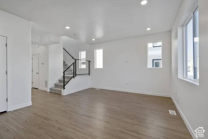 Wood-finish flooring, recessed lighting, white walls, and a staircase with black metal railing