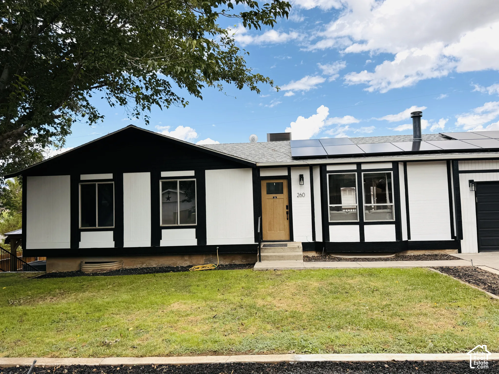 Modern ranch-style residence featuring a contrasting black and white exterior, solar panel installation, a natural wood-finish front door, and a black garage door