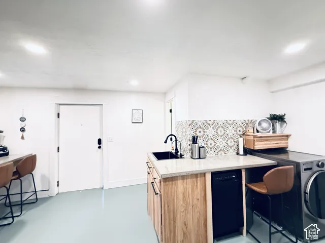 Kitchenette featuring light-toned wood-finish cabinetry, a black sink, and a patterned tile backsplash