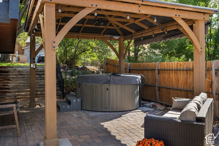 Expansive patio featuring a wooden gazebo, string lighting, and a built-in hot tub with steps