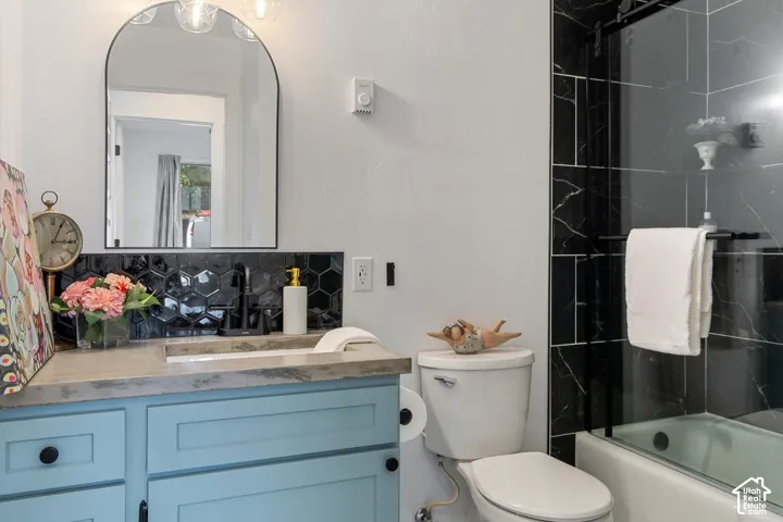 Arched vanity mirror, black hexagonal tile backsplash, concrete-finish vanity countertop, light blue vanity cabinetry, and a shower-tub combination with black-veined tile surround