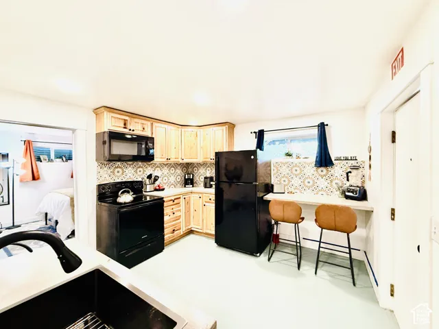 Kitchen featuring light wood cabinetry, black appliances, patterned tile backsplash, and light-toned flooring