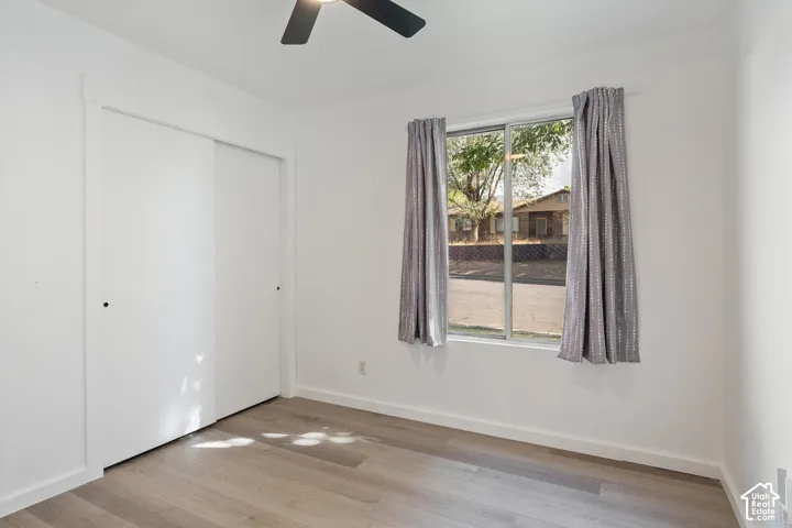 Bright room with wood-finish flooring, a ceiling fan, and sliding closet doors