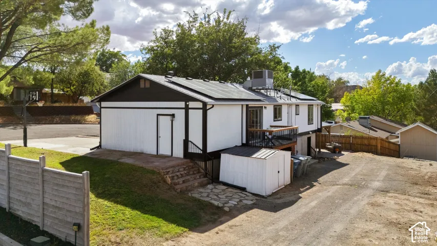 Single-story dwelling with a lower-level deck, dark roof, solar panels, and white siding