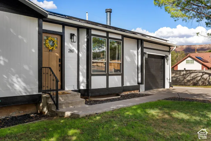 Exterior with white siding, black trim, and a wood-finish front door with a black wrought iron railing