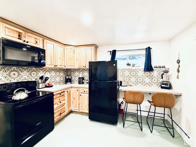 Corner kitchen featuring wood cabinetry, patterned tile backsplash, and a black range