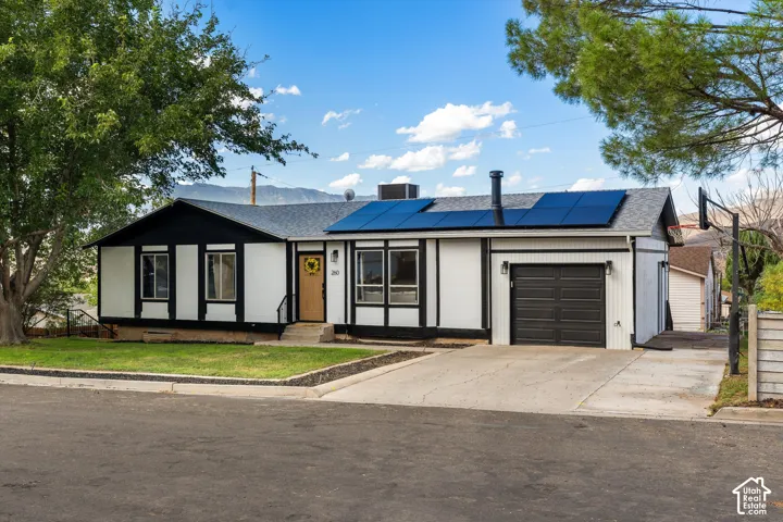 Single-story residence featuring a gray shingled roof with solar panels, an attached single-car garage, and a concrete driveway