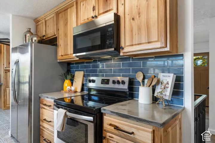 Stainless steel appliances, wood cabinetry, dark subway tile backsplash, and light-toned countertops