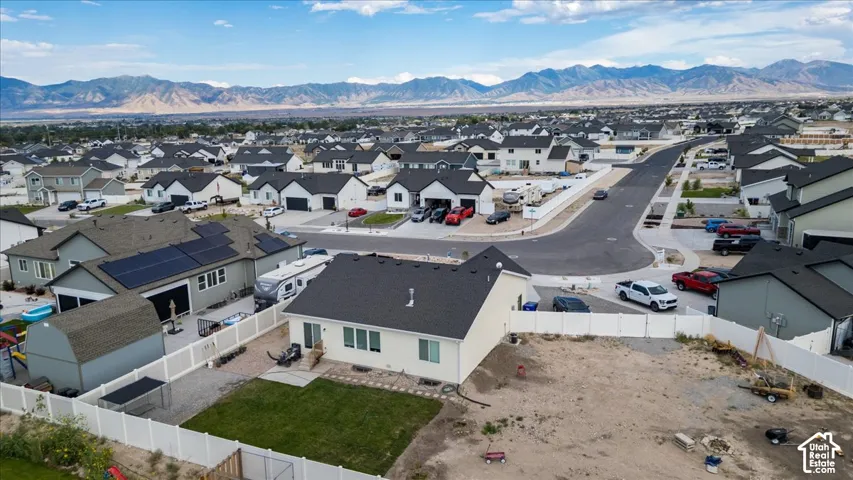 Expansive residential area with mountain backdrop, featuring a manicured lawn, white fencing, and solar panels on an adjacent property