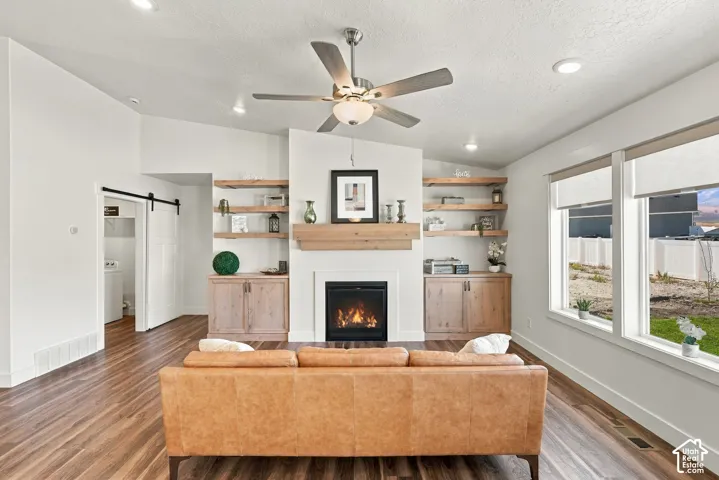 Fireplace with wood mantle, built-in shelving, wood-finish flooring, ceiling fan, and large windows