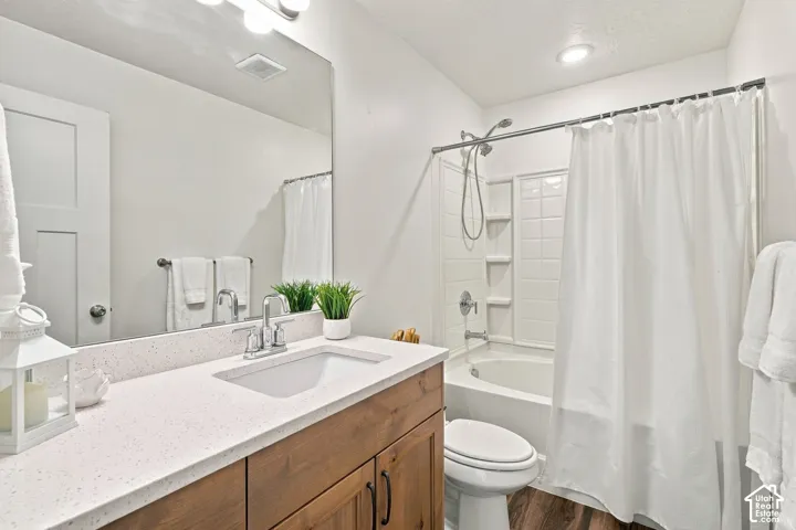Wood-finish flooring, white vanity with an undermount sink, quartz countertop, and a white tub with subway tile surround
