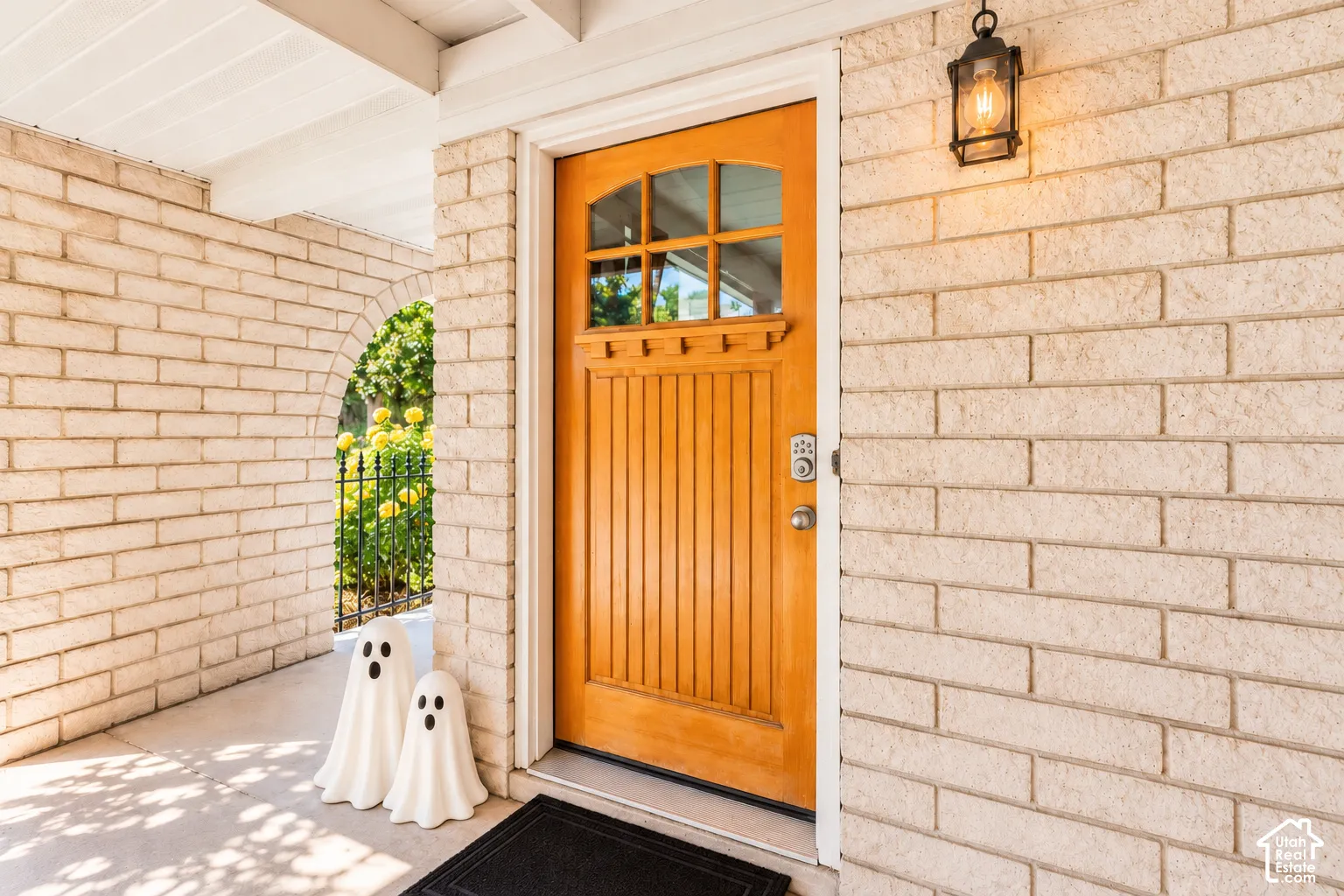 Brick exterior with an arched entryway, natural wood paneled door with window accents, and an exterior wall lantern
