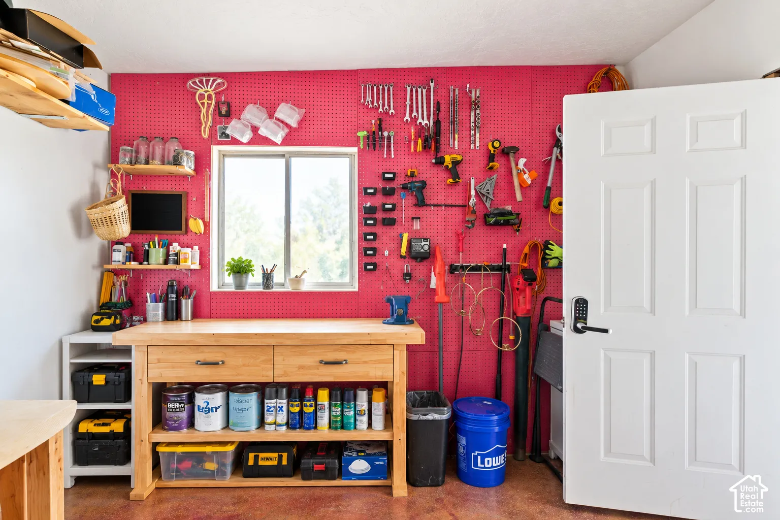 Workbench with integrated shelving and drawers, window with natural light, pegboard wall system, white paneled door, and recessed lighting