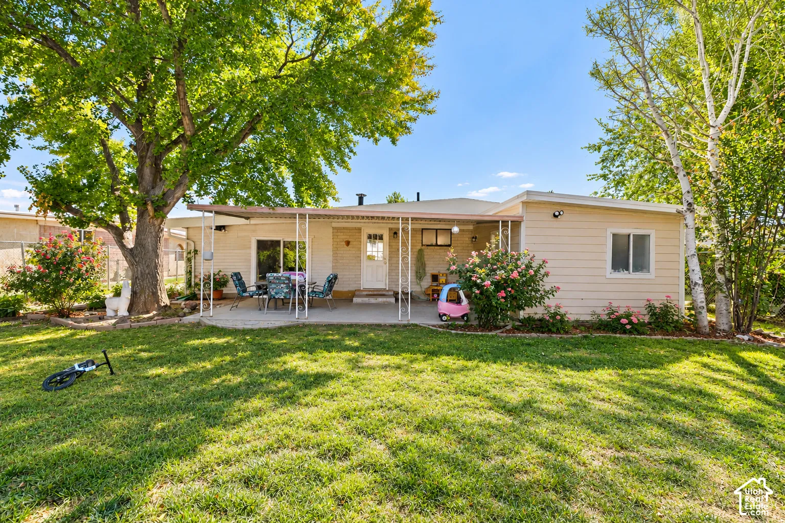 Expansive grass lawn with mature trees, offering a concrete patio with a covered awning