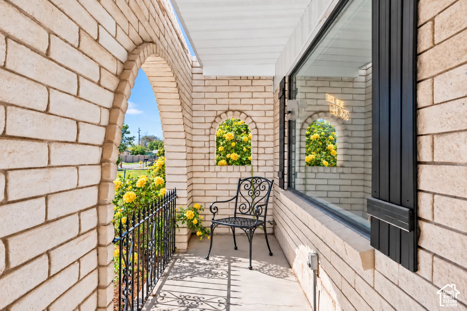 Brick exterior with arched entryway, concrete flooring, black wrought-iron railing, and large window with dark shutters