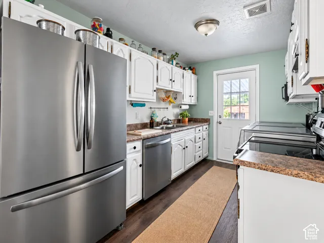 Kitchen featuring stainless steel appliances, wood-finish flooring, white cabinetry, a single basin sink, and a glass-paneled exterior door