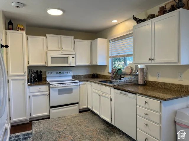 White cabinetry, integrated microwave, built-in dishwasher, and a window with blinds