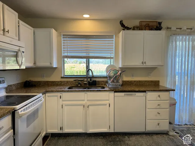 Kitchen featuring white cabinetry, dark speckled countertops, and an undermount sink with a gooseneck faucet