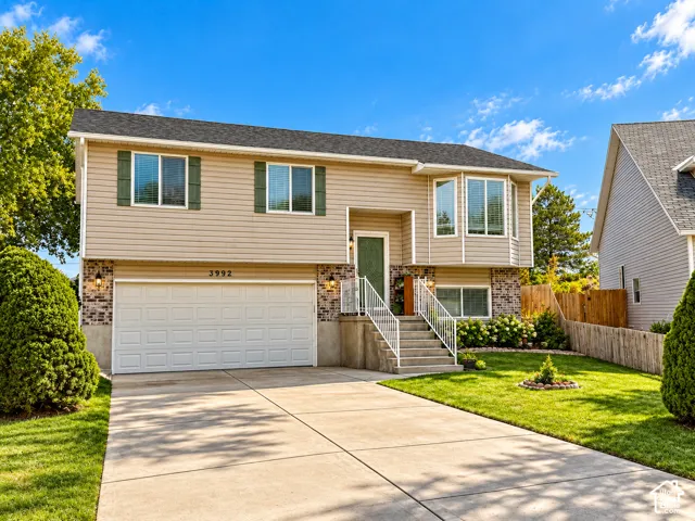 Split-level residence featuring a two-car garage, concrete driveway, and established landscaping