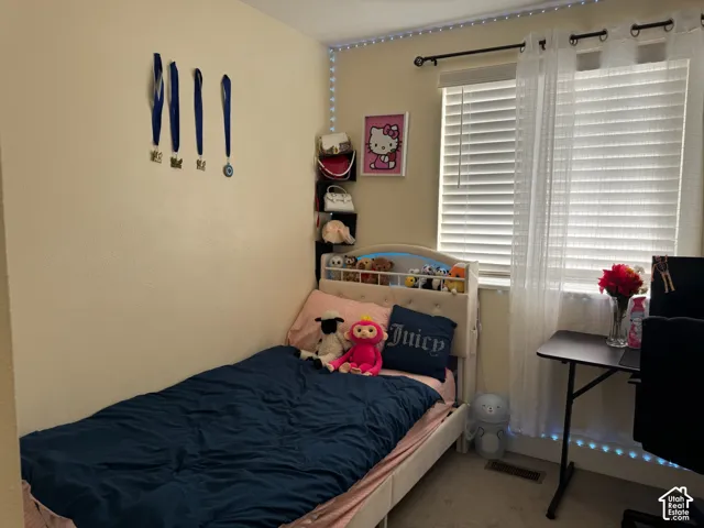 Carpeted bedroom with a window featuring blinds and sheer curtains