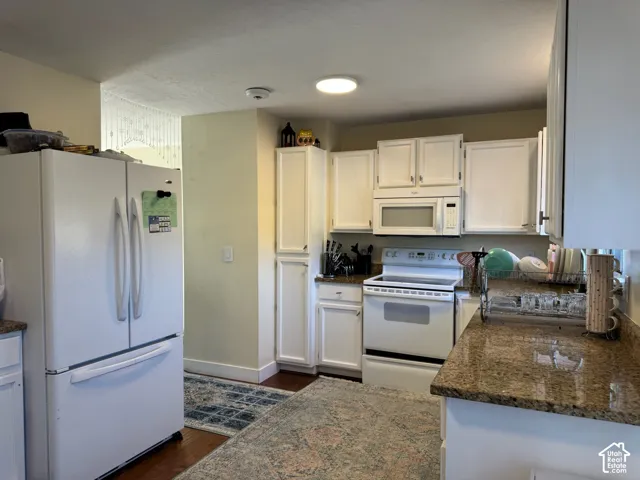 White cabinetry, stone-finish countertops, white appliances, and wood-finish flooring