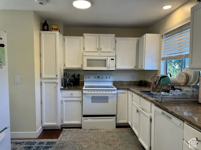 White cabinetry with chrome hardware, granite-style countertops, and white appliances