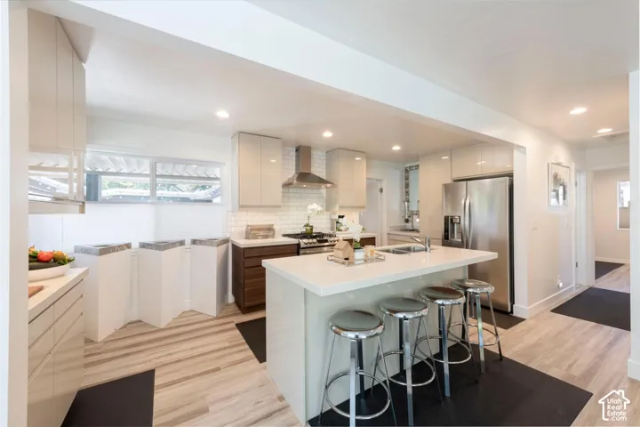 Kitchen featuring light wood-finish flooring, white countertops, white subway tile backsplash, stainless steel appliances, and a central island with integrated sink
